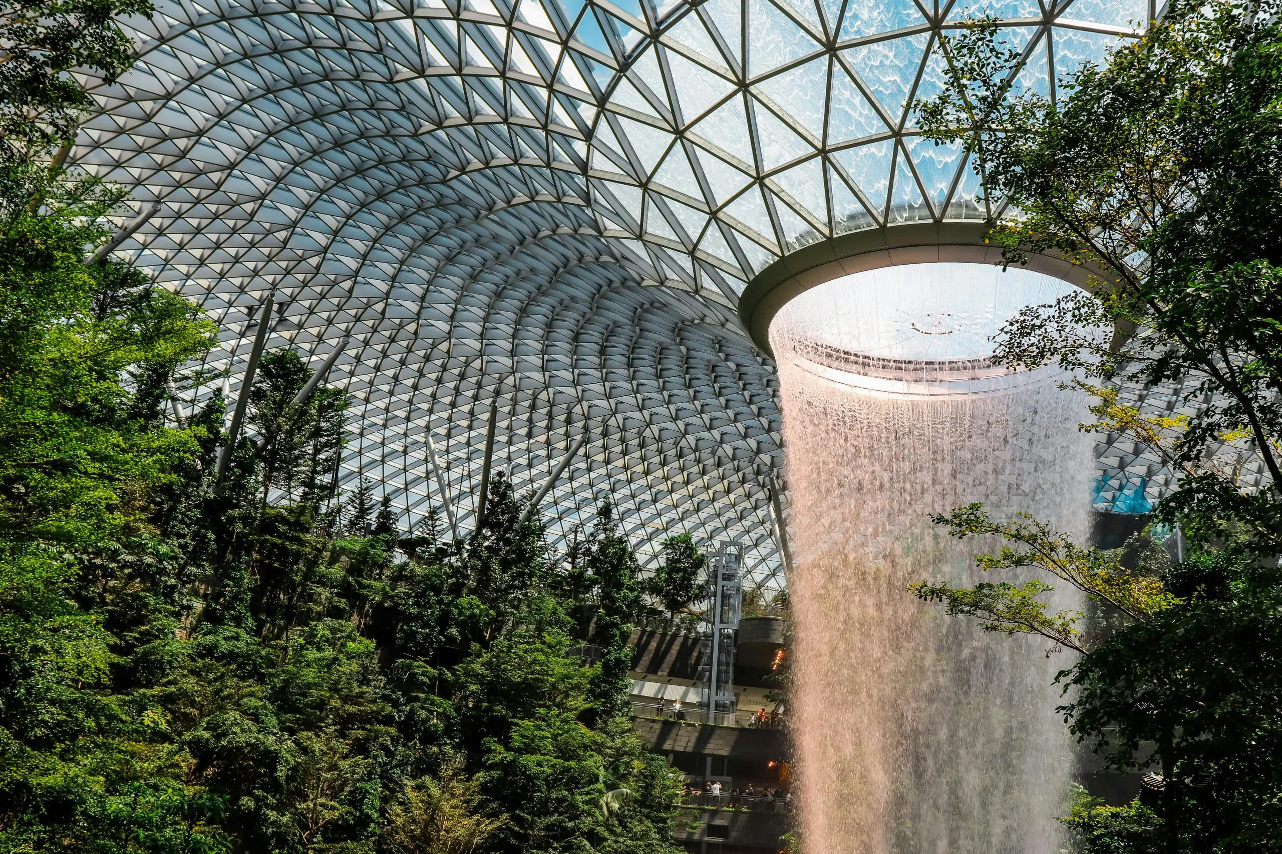 Indoor waterfall surrounded by lush greenery under a glass dome at Jewel Changi Airport in Singapore.