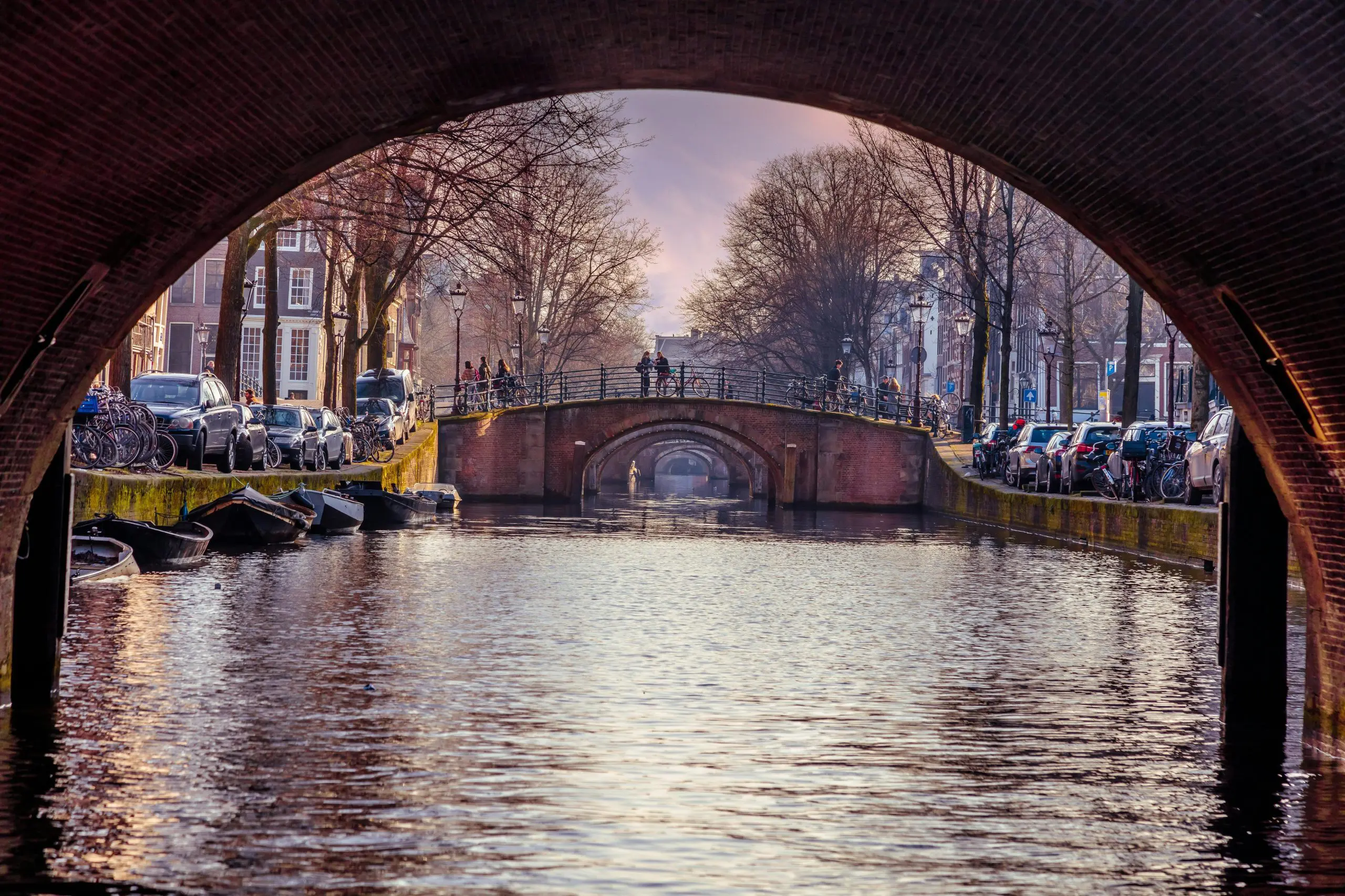 Scenic view of Amsterdam’s canals framed by brick bridges and bicycles, capturing the charm and lifestyle of expats in the Netherlands.