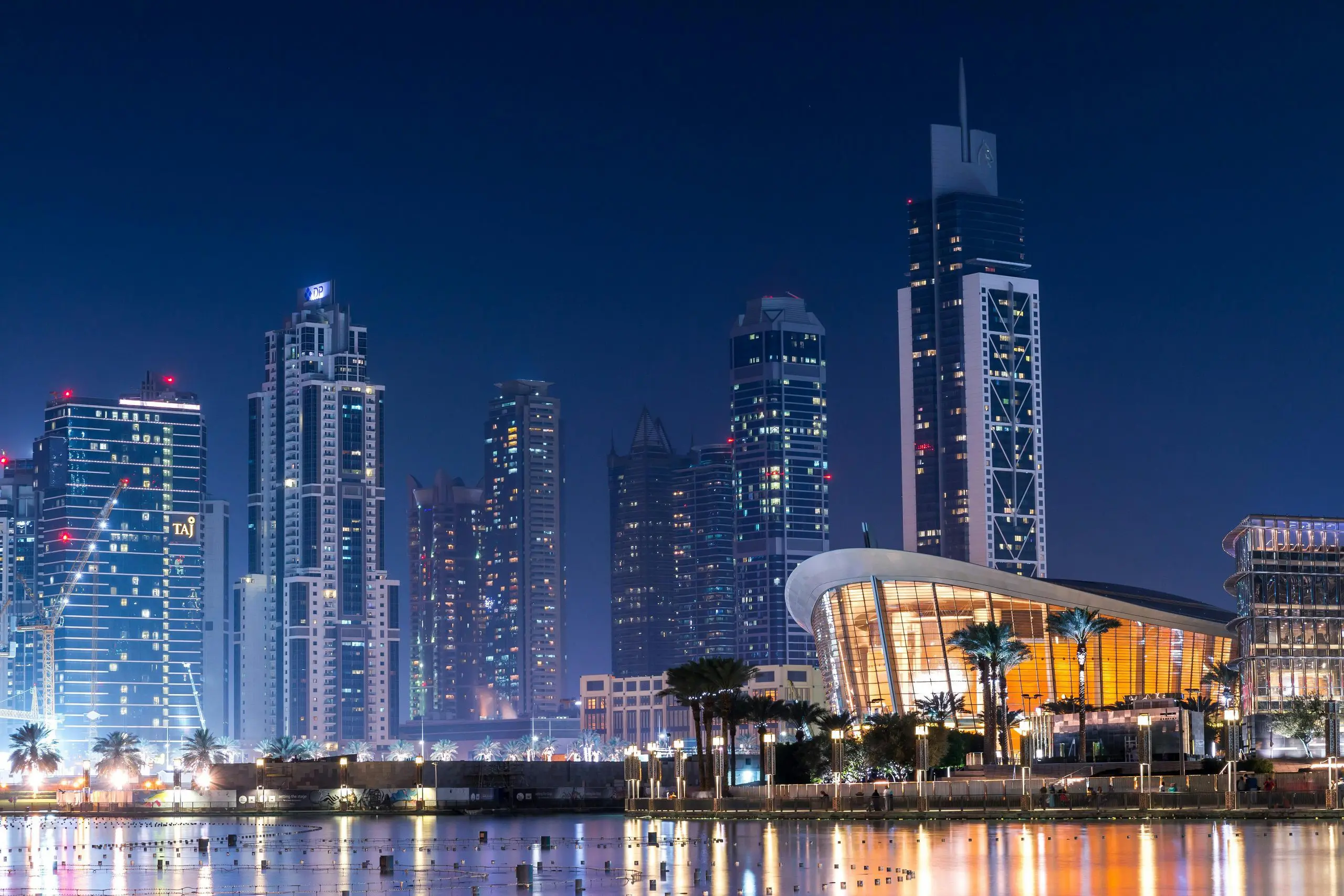 Night view of Dubai skyline with illuminated skyscrapers reflecting on the water, representing modern city life for expats in the UAE.