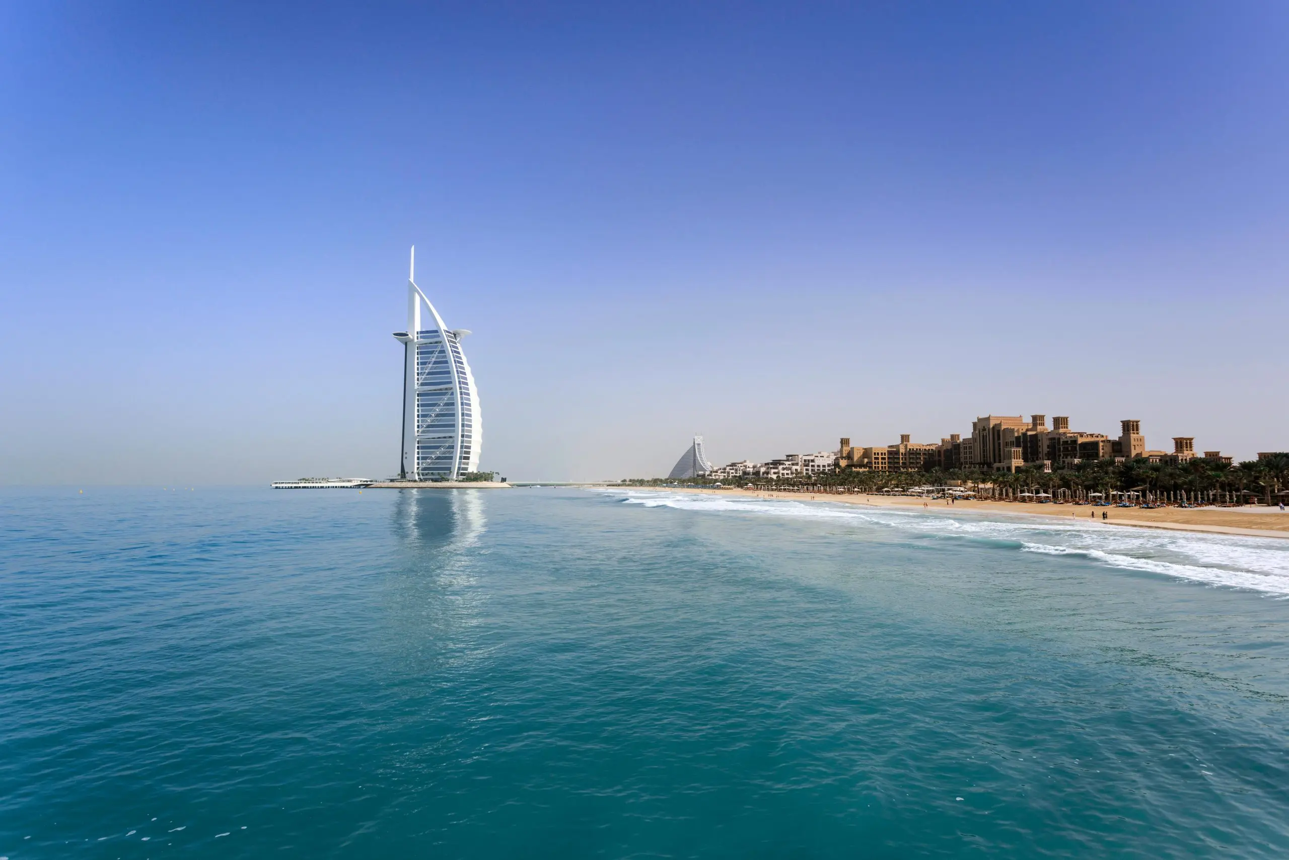 Scenic view of Burj Al Arab by the Dubai coastline under a clear blue sky, symbolizing luxury living and expat destinations in the UAE.