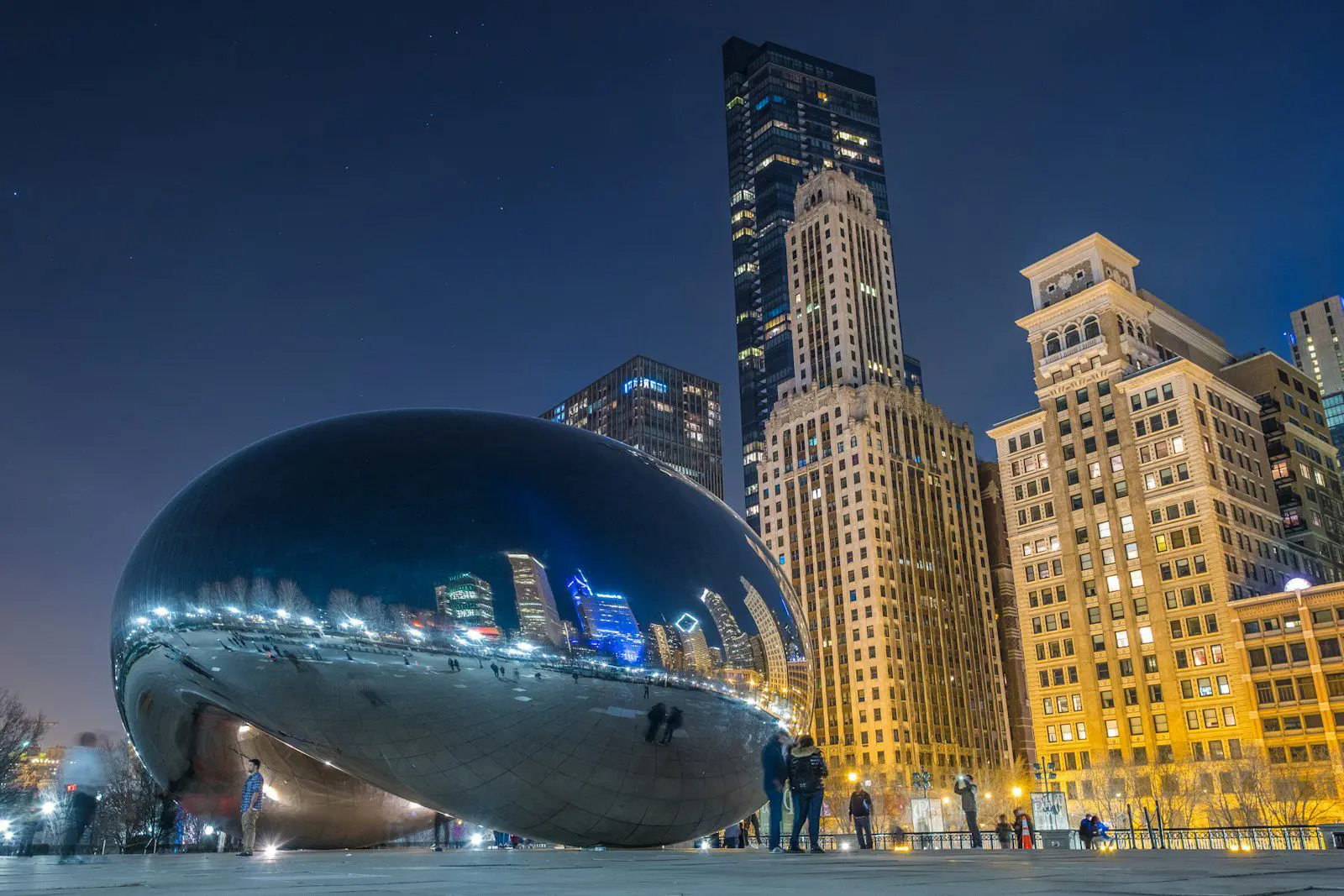Photo by Lance Anderson Cloud Gate sculpture in Millennium Park, Chicago illuminated at night surrounded by skyscrapers representing Illinois city life.
