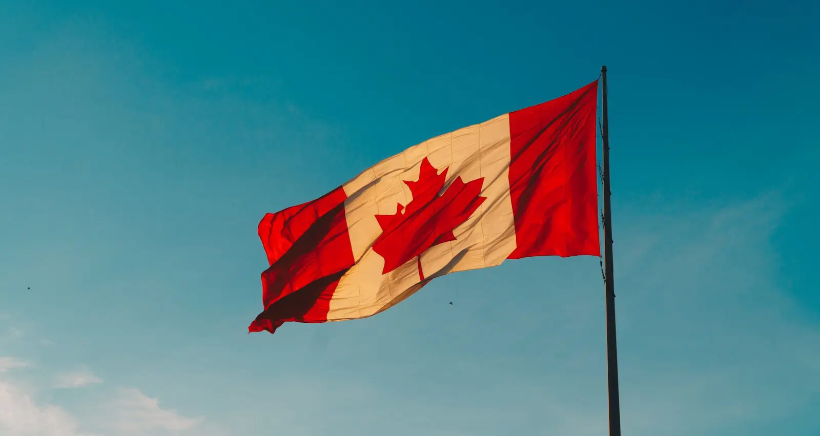 Canadian flag waving under blue sky, symbolizing immigration and expat life in Canada.