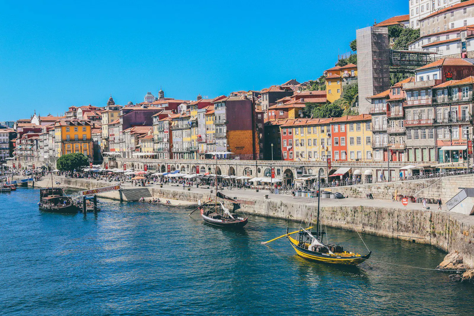 Vibrant waterfront in Porto, Portugal, with boats and colorful houses, representing the relaxed lifestyle for expats in Portugal.