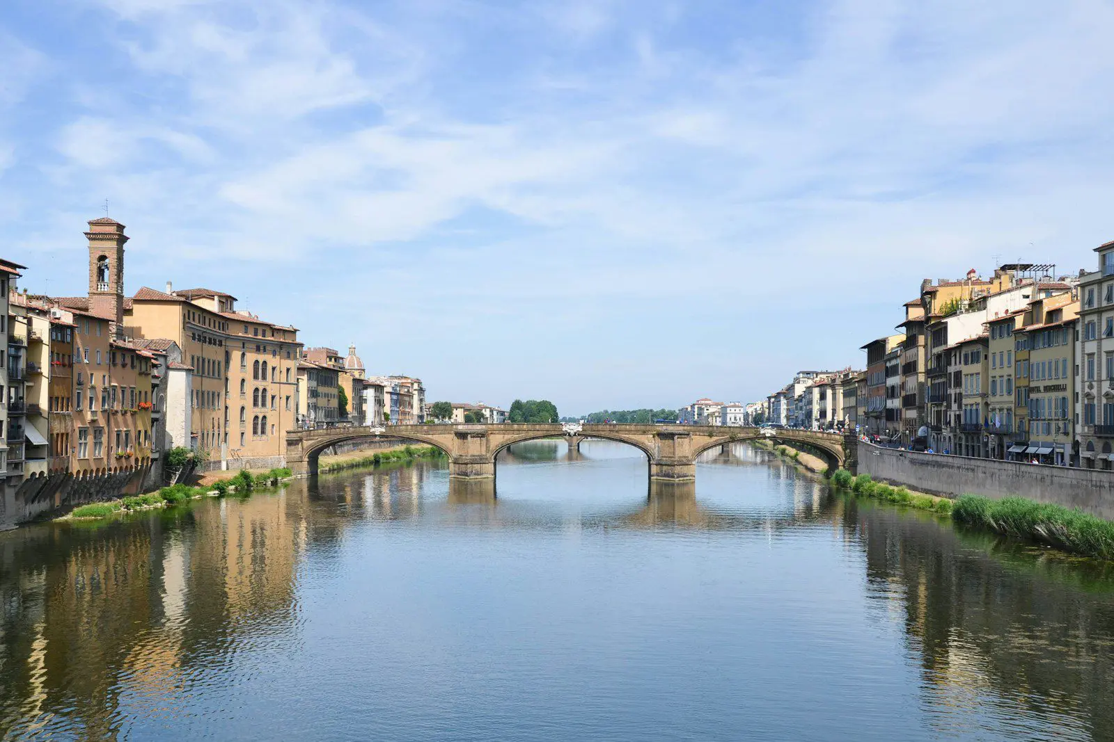 View of Ponte alla Carraia bridge over the Arno River in Florence surrounded by colorful historic buildings.