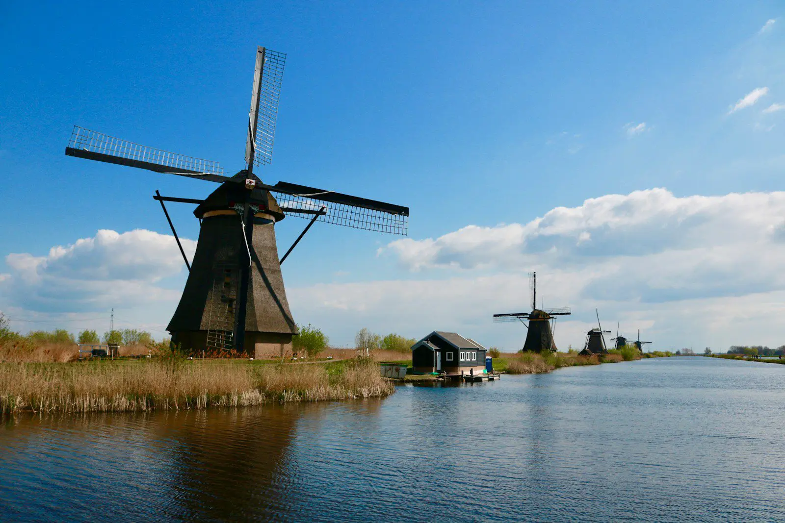 Traditional Dutch windmills along the canal at Kinderdijk under a bright blue sky in the Netherlands.