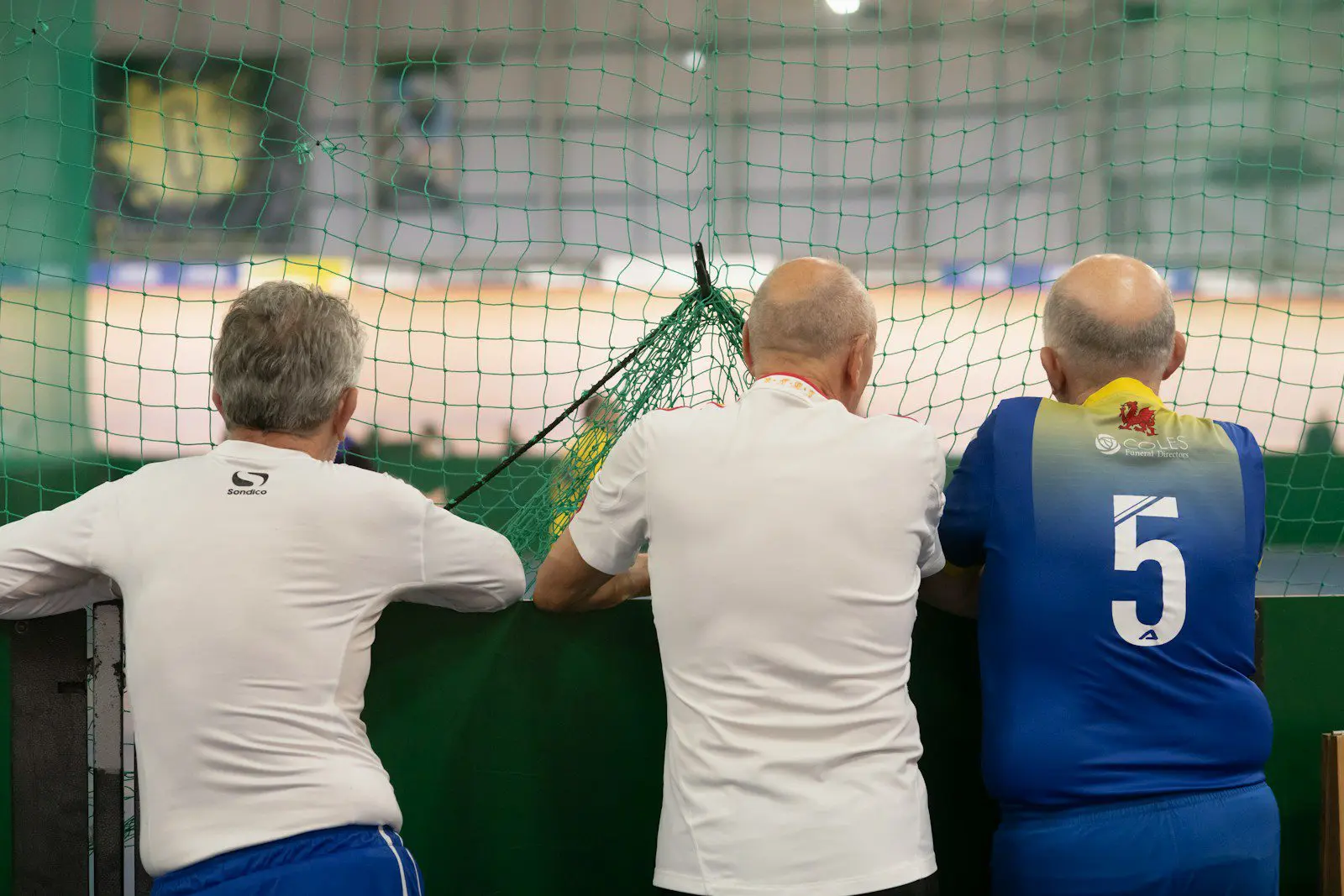 Photo by Age Cymru Three senior men watching an indoor walking football match, symbolizing active aging and social fitness for older expats.