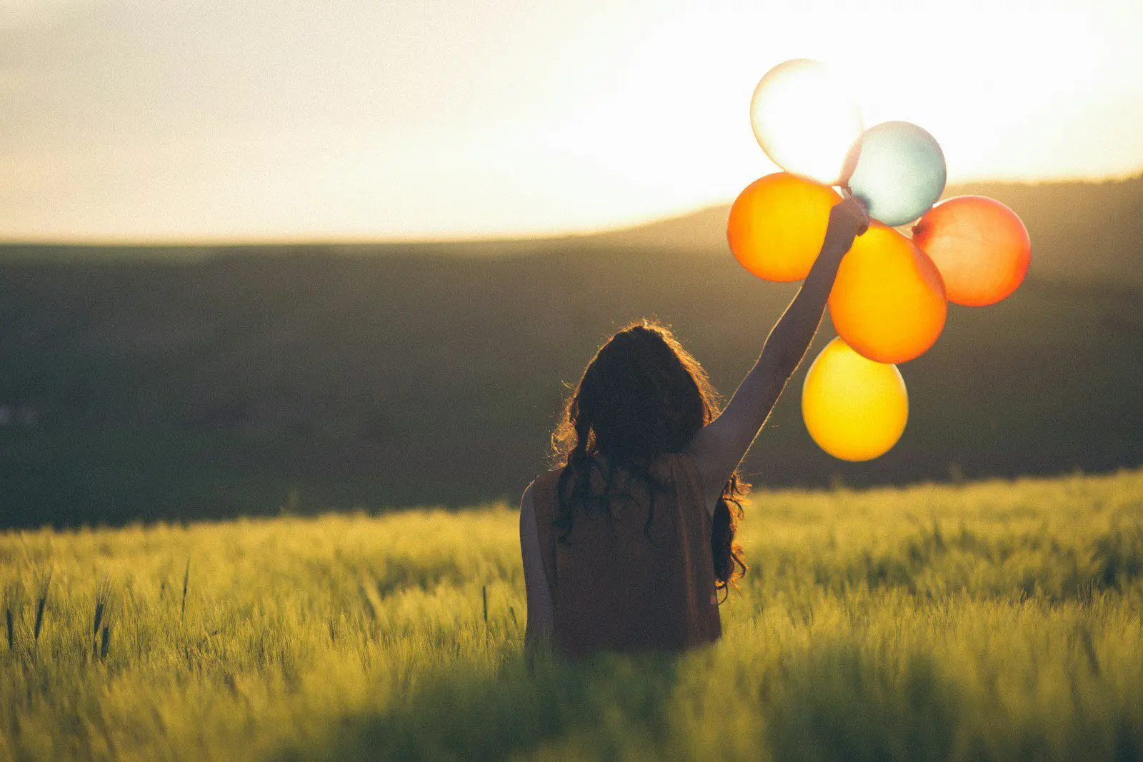 Photo by Catalin Pop Expat woman holding bright balloons in a sunlit field, symbolizing self-acceptance and body positivity while living abroad.