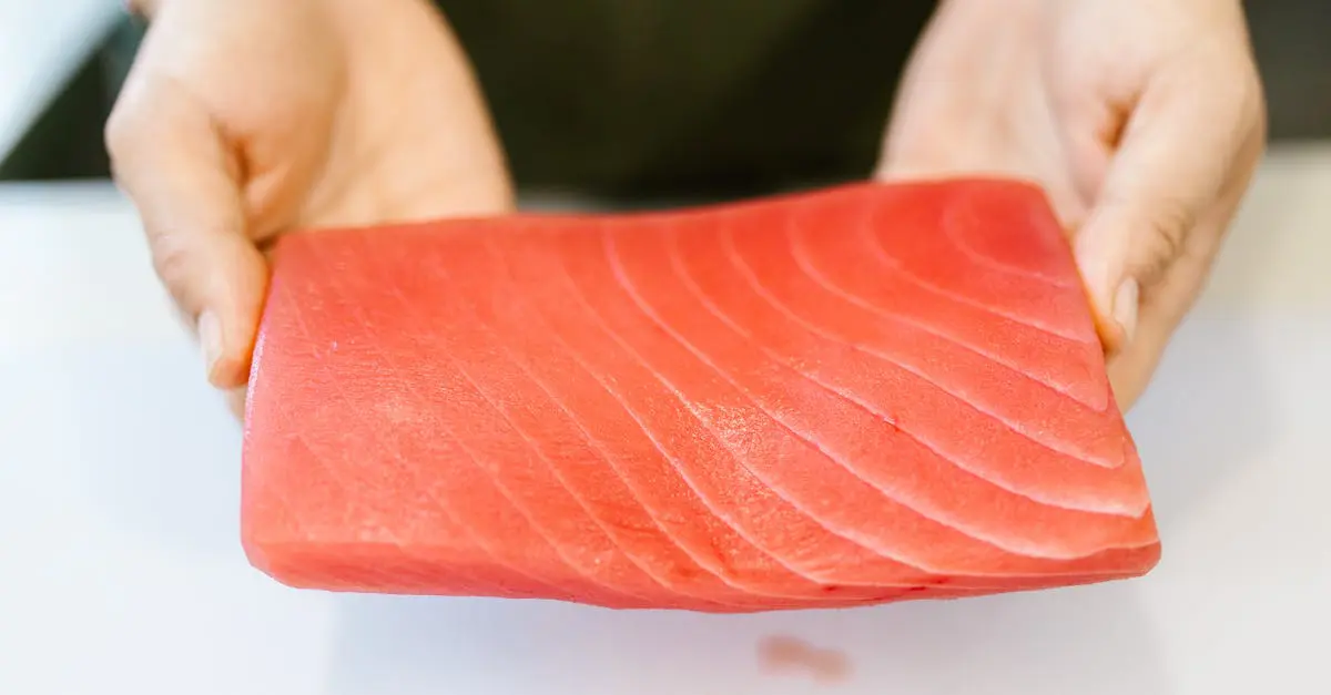 Close-up of a person holding a fresh cut of raw tuna, symbolizing healthy protein sources and balanced nutrition for expat diets.