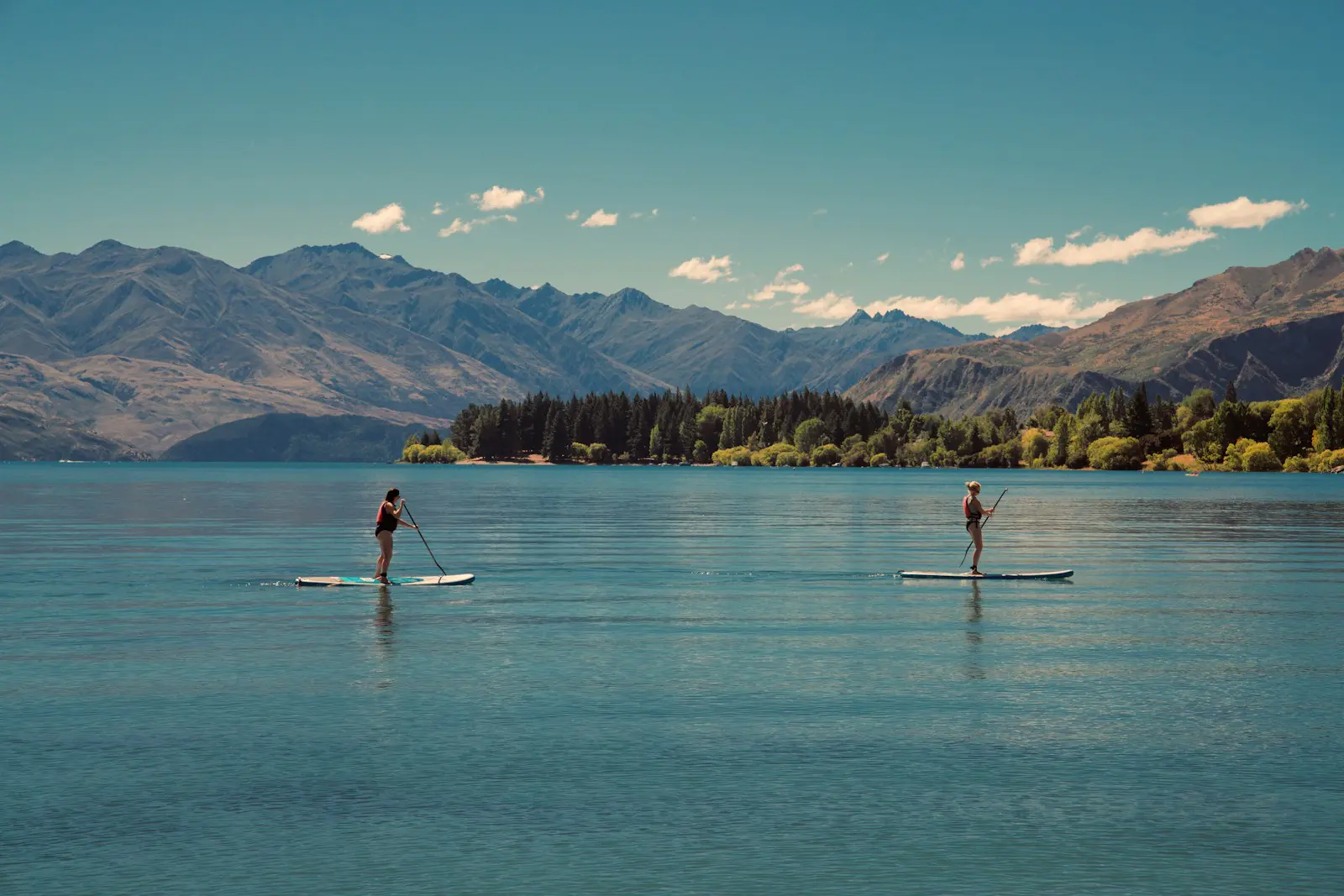 Two people paddleboarding on calm lake surrounded by mountains representing outdoor fitness, mindfulness, and expat adventure lifestyle.